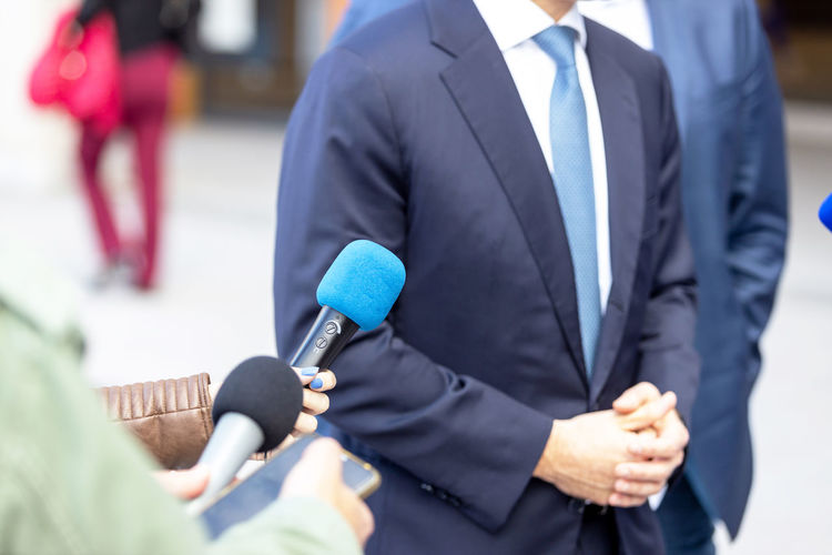 Journalists with microphones interviewing politician or business person during media event