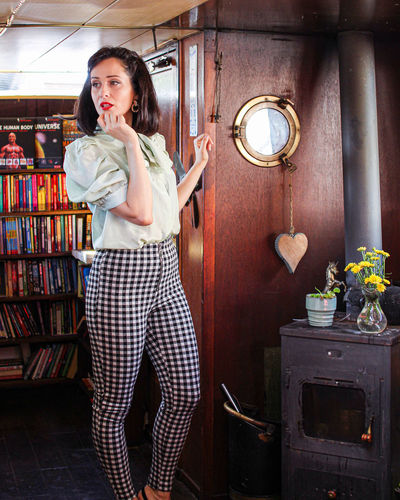 Portrait of woman standing against wall in front of library and fireplace