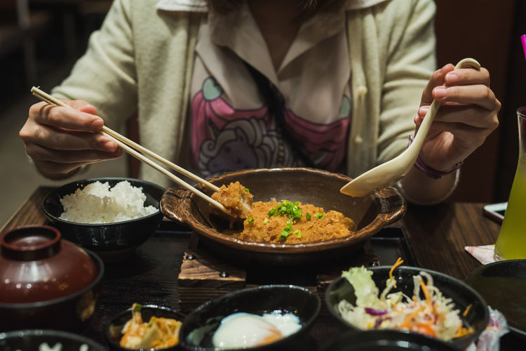 Close-up midsection of woman having meal with chopsticks at table