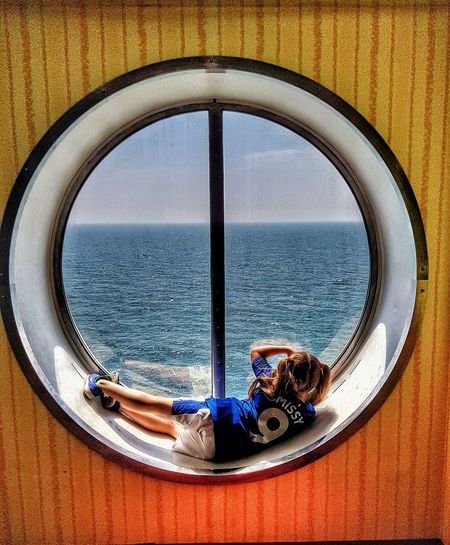 Rear view of girl looking at sea through porthole window