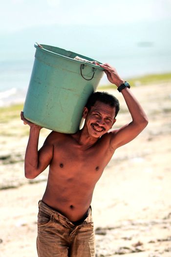 Portrait of smiling man carrying garbage bin on shoulder