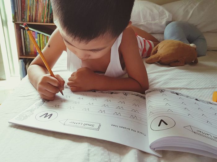 Boy writing homework while lying on bed at home