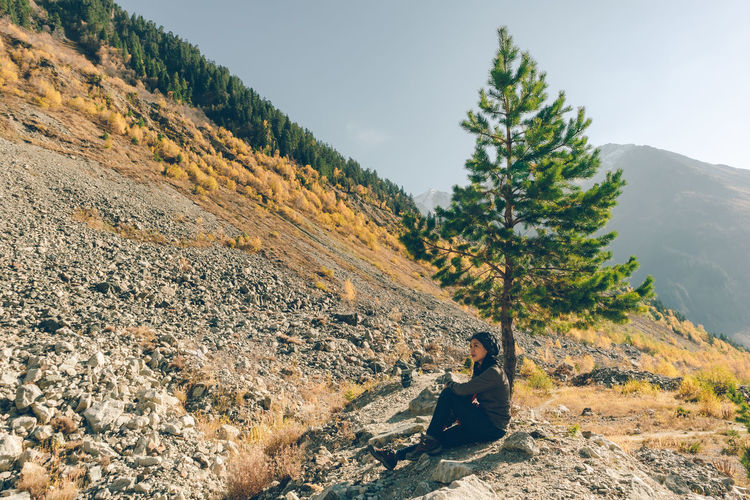 Woman sitting on mountain against clear sky during sunny day