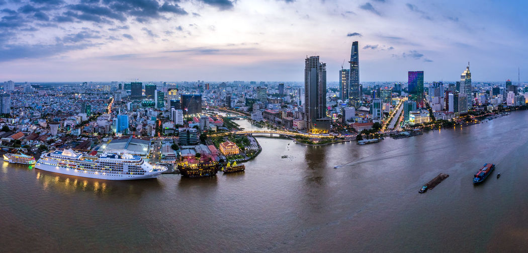 Aerial view of cityscape by river against cloudy sky
