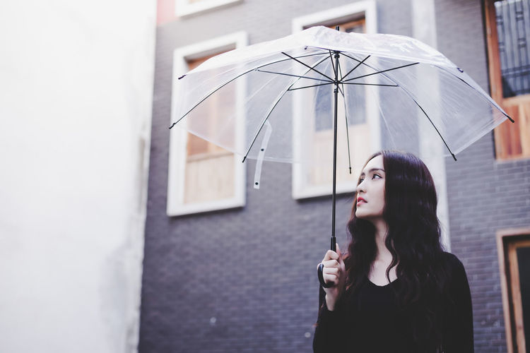 Young woman standing with umbrella against building