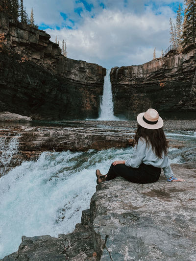 Woman sitting on rock by waterfall