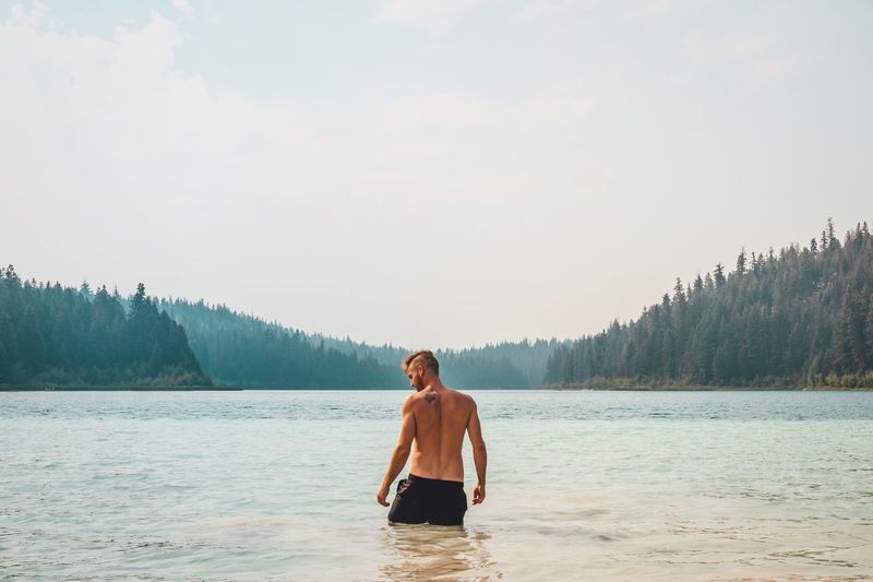 Shirtless man standing in lake against clear sky