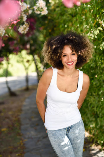 Portrait of cheerful young woman standing at public park