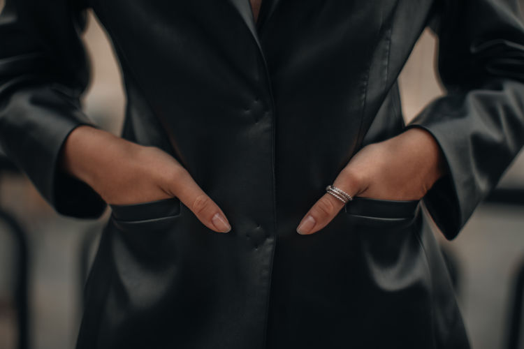 Female hands with silver rings in the pockets of a black long leather jacket. jewelry