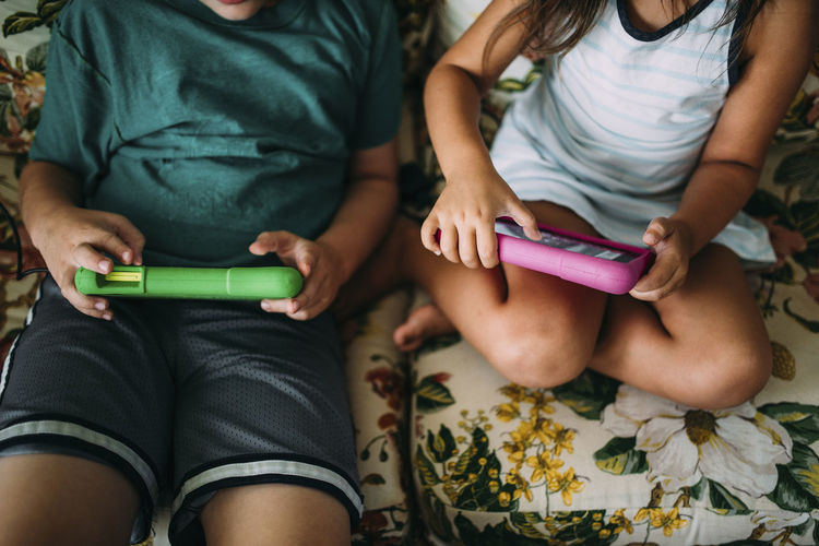 Cropped image of siblings playing video game while sitting on sofa at home