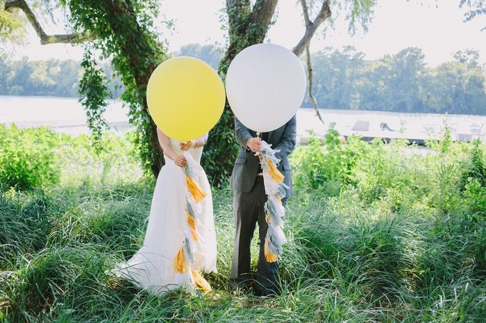 Bride and bridegroom standing with balloons in front of face on grass