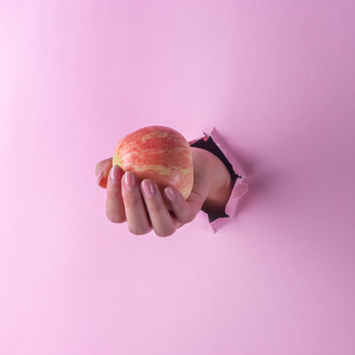 Close-up of hand holding apple while coming out from torn paper 