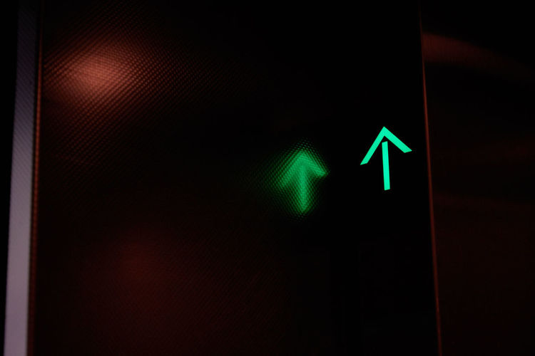 Low angle view of illuminated green arrow with reflection in dark elevator