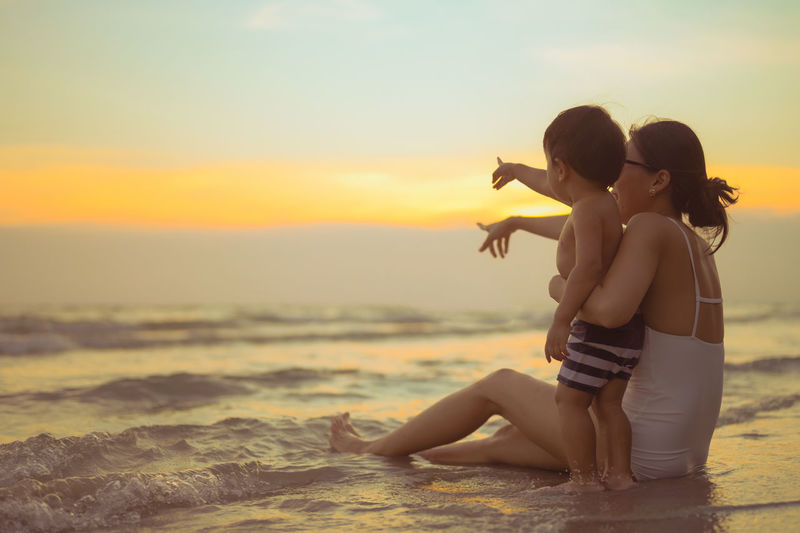 Couple kissing on beach against sky during sunset