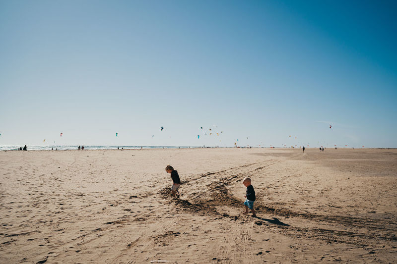 Kids running at the beach with kitesurfers in the back riding kites