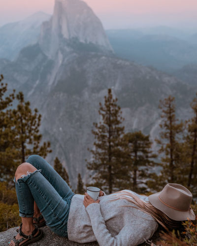 Full length side view of woman lying on rock against mountains