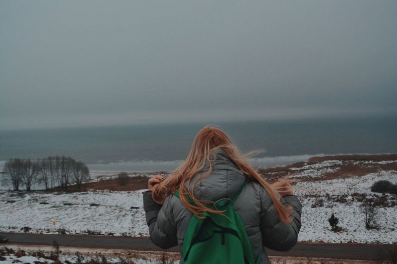 Rear view of woman looking at sea against sky during winter