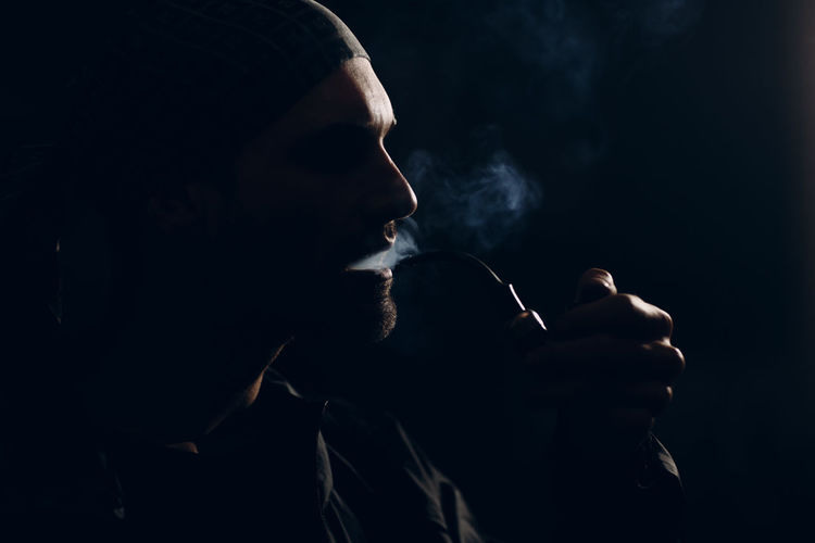 Side view of young man smoking cigarette against black background