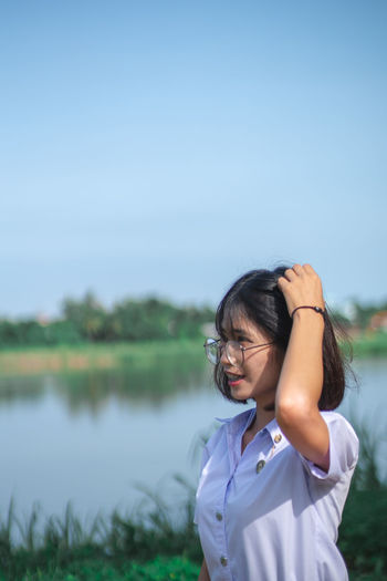Woman standing by lake against clear blue sky
