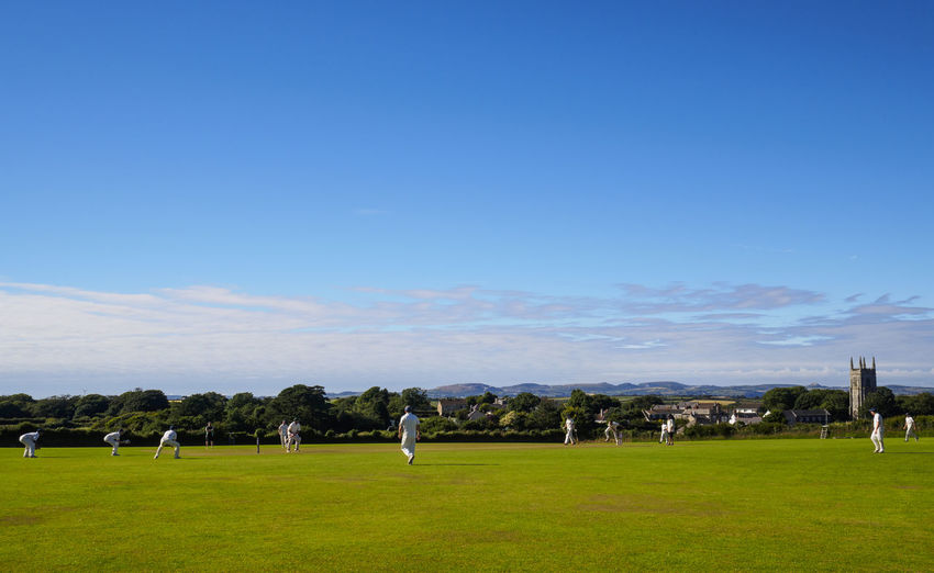 Men playing cricket on field against sky