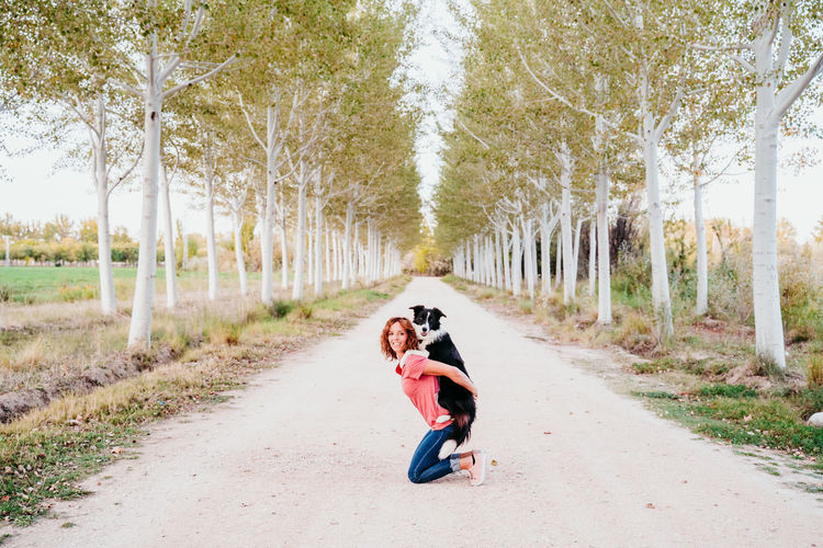 Woman carrying dog on road amidst trees in forest
