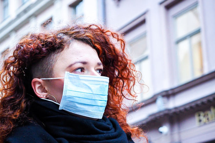 Woman wearing mask looking away against building