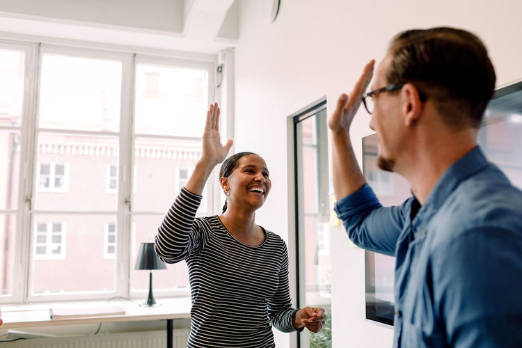 Happy businesswoman giving high-five to male colleague in office