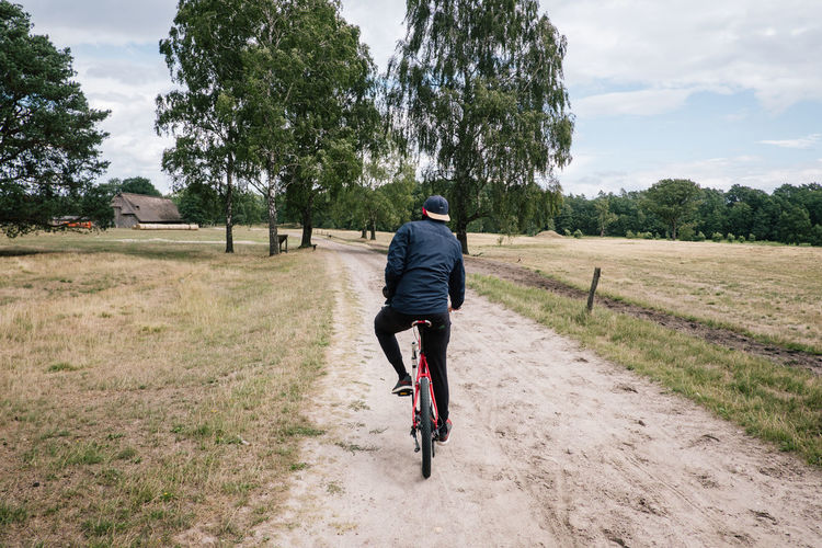 Rear view of man riding bicycle on dirt road amidst field