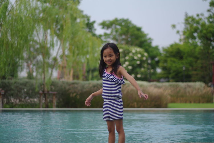 Portrait of a cute asian girl standing in the pool on a clear day. happily