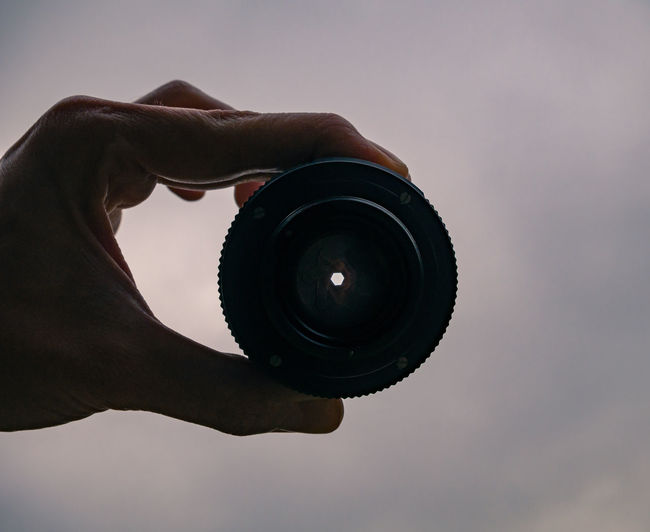 Close-up of hand holding camera against sky