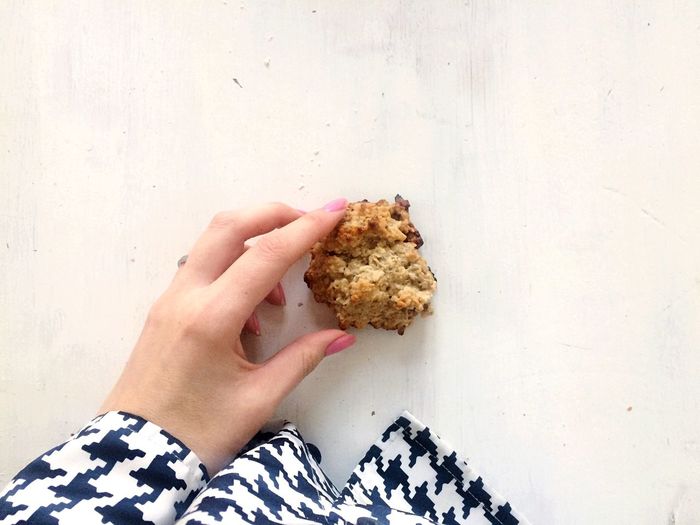 Cropped hand of woman holding cookie on white table