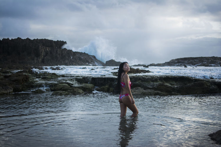 Woman stands in water on a rocky beach with tidepools