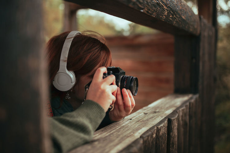 Close-up of woman wearing headphones photographing through window