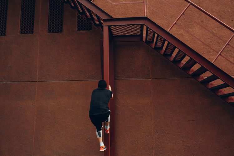 Man climbing on metal column against brown wall