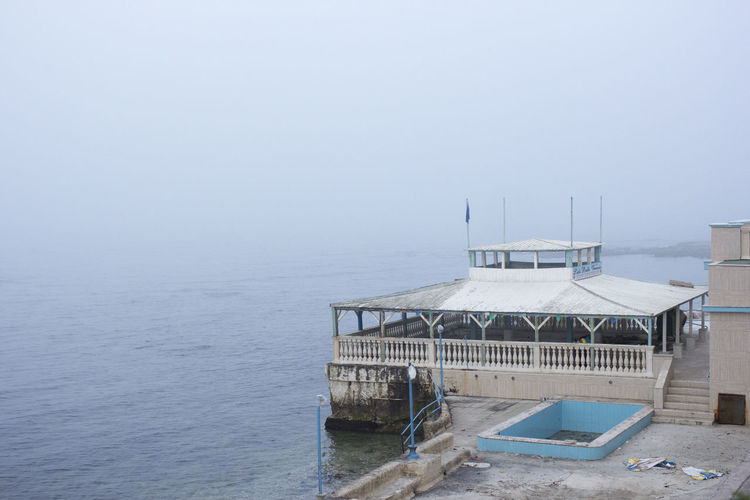 Built structure by sea against sky during foggy weather