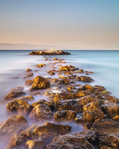 Rocks at seashore against sky during sunset