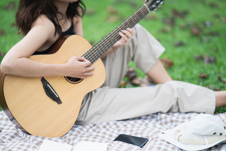 Midsection of girl playing guitar while sitting outdoors