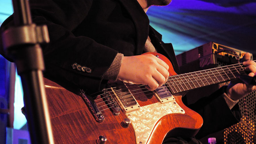 Midsection of man playing electric guitar during music concert