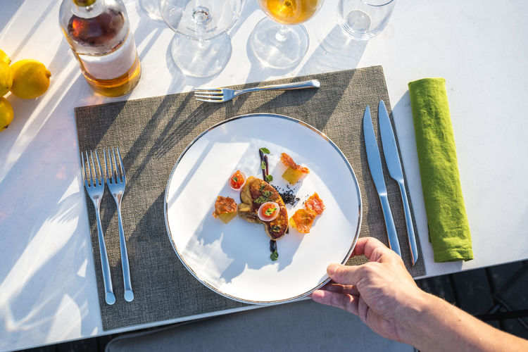Waiter serving well garnished fried goose liver dish at outdoor high cuisine restaurant