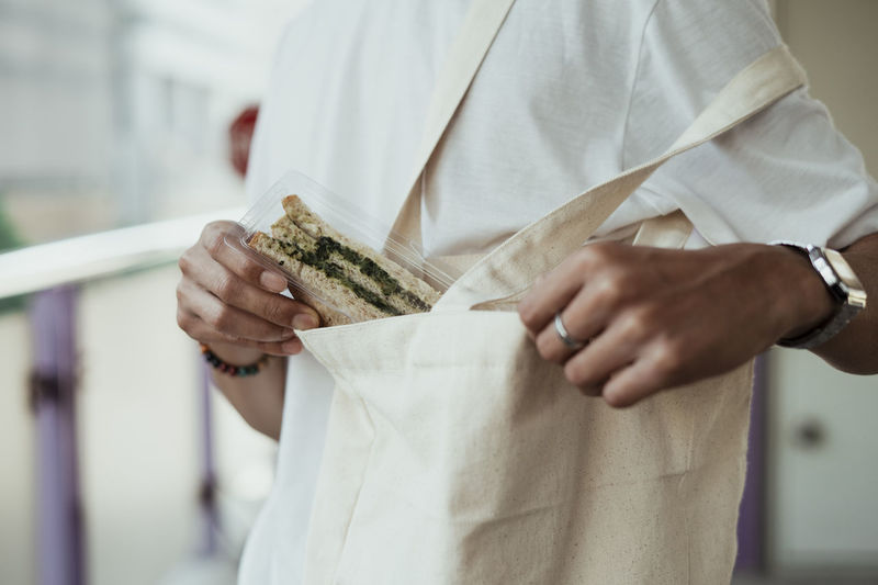 Midsection of person putting sandwich in bag
