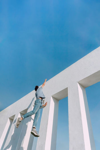 Low angle view of man working on building against blue sky