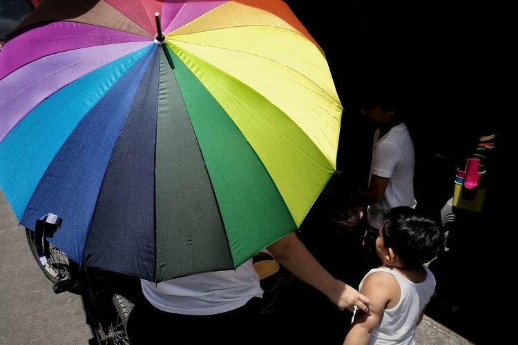 Rear view of people standing against multi colored umbrella
