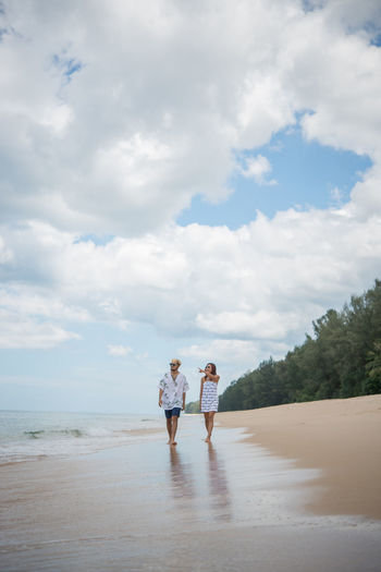 Man and woman walking at beach against sky
