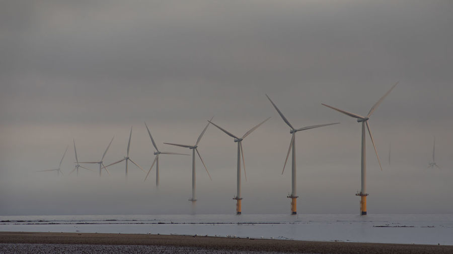 Wind turbines on beach against sky