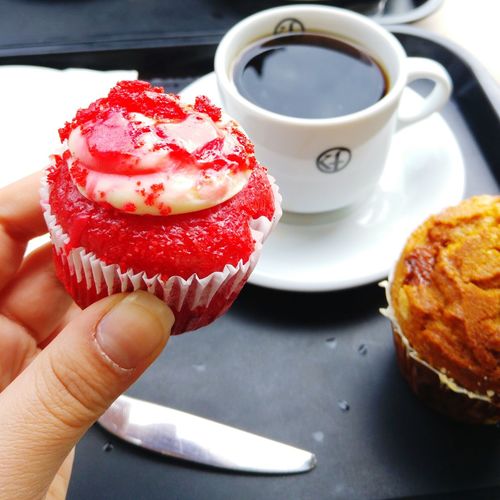 Cropped image of person holding red cupcake by coffee in tray