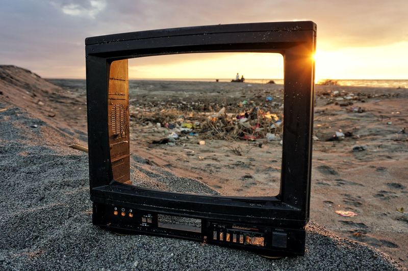 Close-up of old abandoned television set on land during sunset