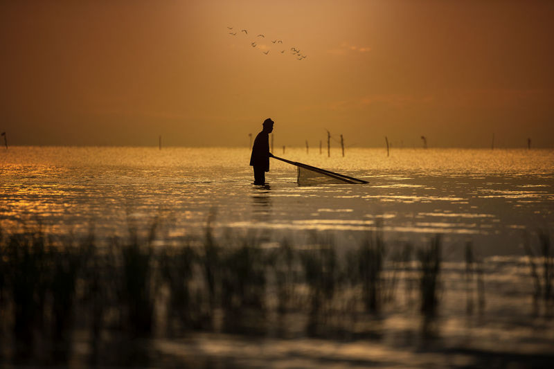 Silhouette man fishing in sea against sky during sunset