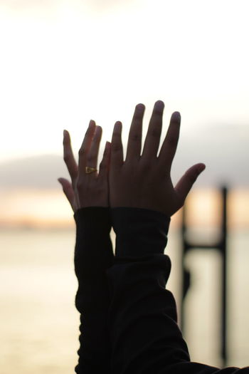 Close-up of hands against sky during sunset