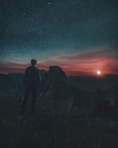 Rear view of man standing on mountain against sky at night
