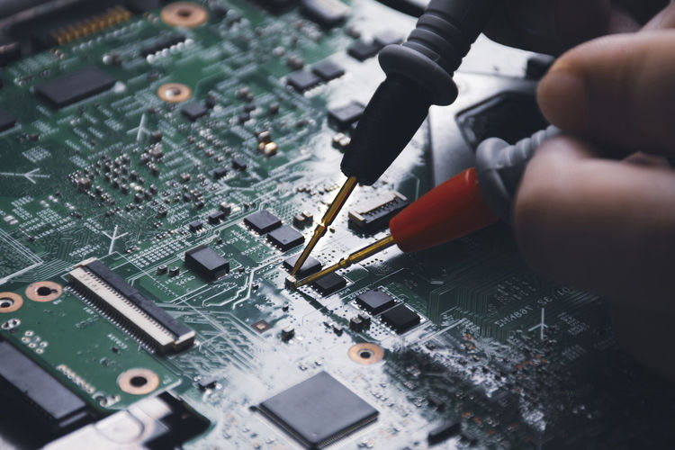 Technician checking laptop circuit board with multimeter